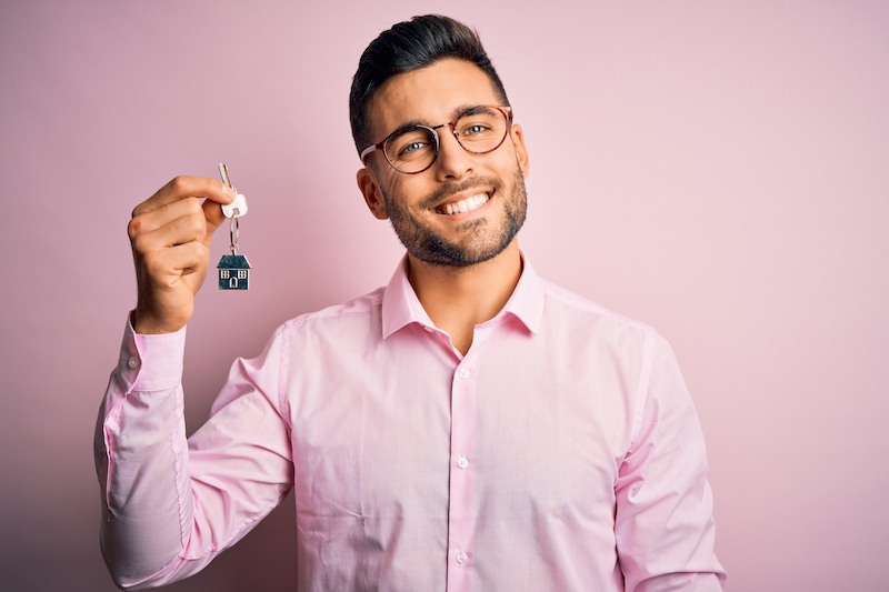 Young real estate business man holding new house keys over pink background with a happy face standing and smiling with a confident smile showing teeth